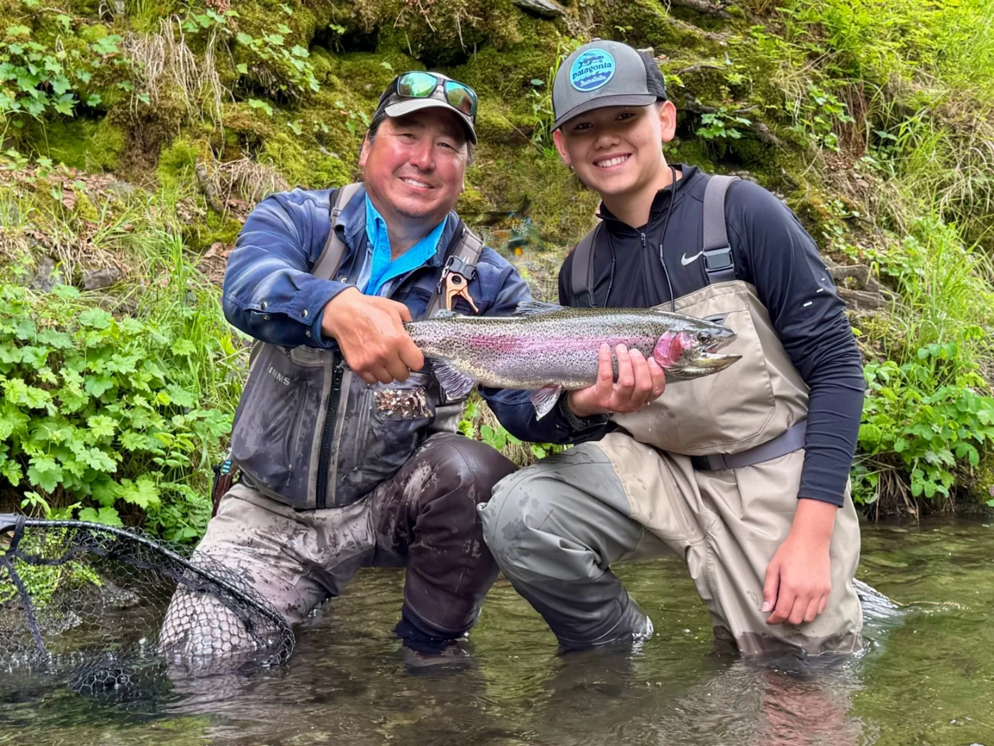 Two anglers wading a Kenai River tributary holding a large rainbow trout, Alaska fly fishing